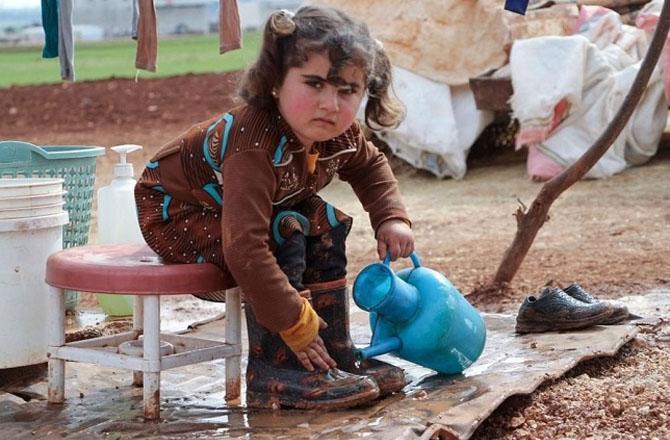 A Syrian refugee girl washes the dirt off her shoes. Photo: X