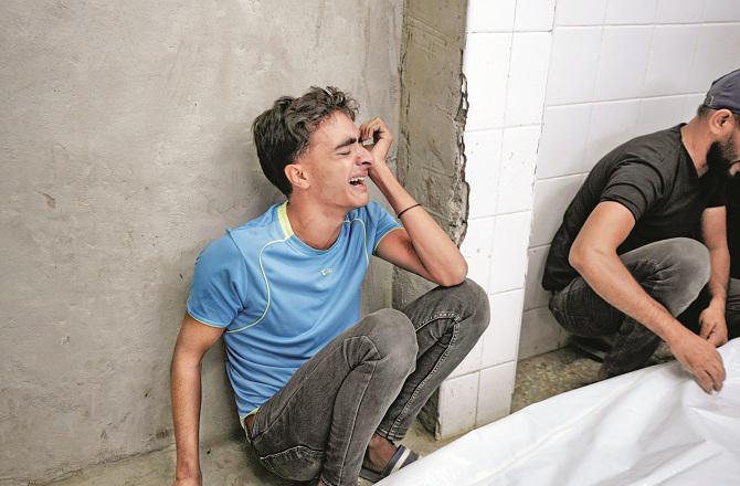 A grieving young man can be seen next to the dead body of his loved one in a hospital in Deir ul-Balah. Photo: INN.